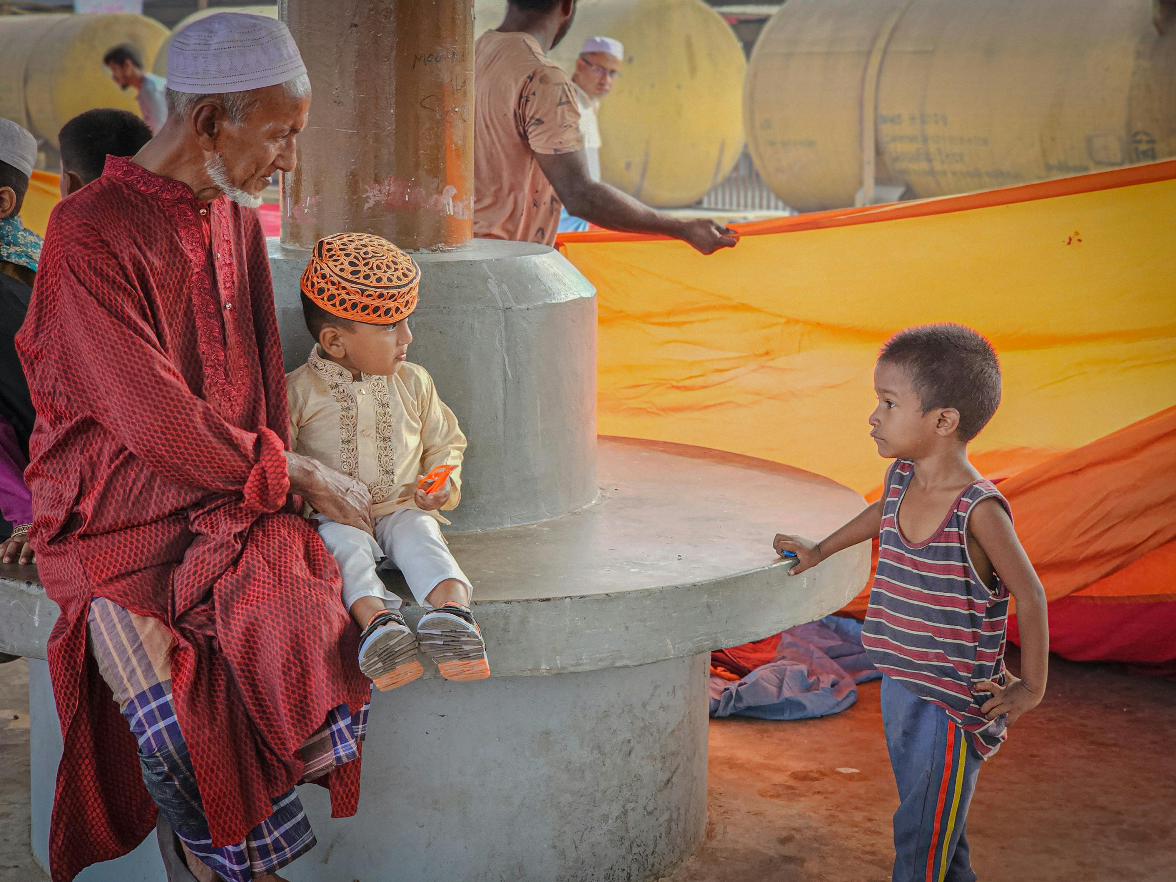 A senior man with children interacts in a vibrant outdoor environment, highlighting cultural attire and vibrant colors.
