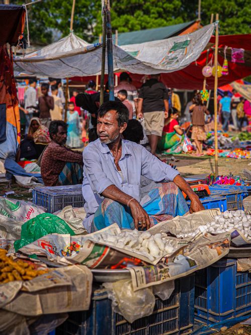 Free A vendor sits at a colorful outdoor market, surrounded by goods and bustling activity. Stock Photo