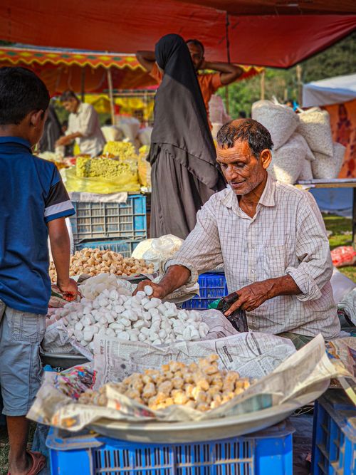 Free Bustling outdoor market scene with a vendor selling fresh produce under a colorful tent. Stock Photo