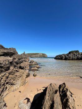 Beautiful rocky beach scene with clear waters under a blue sky in Asturias, Spain.