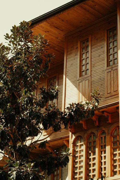Free Capture of traditional wooden house façade with a tree in sunlight. Stock Photo