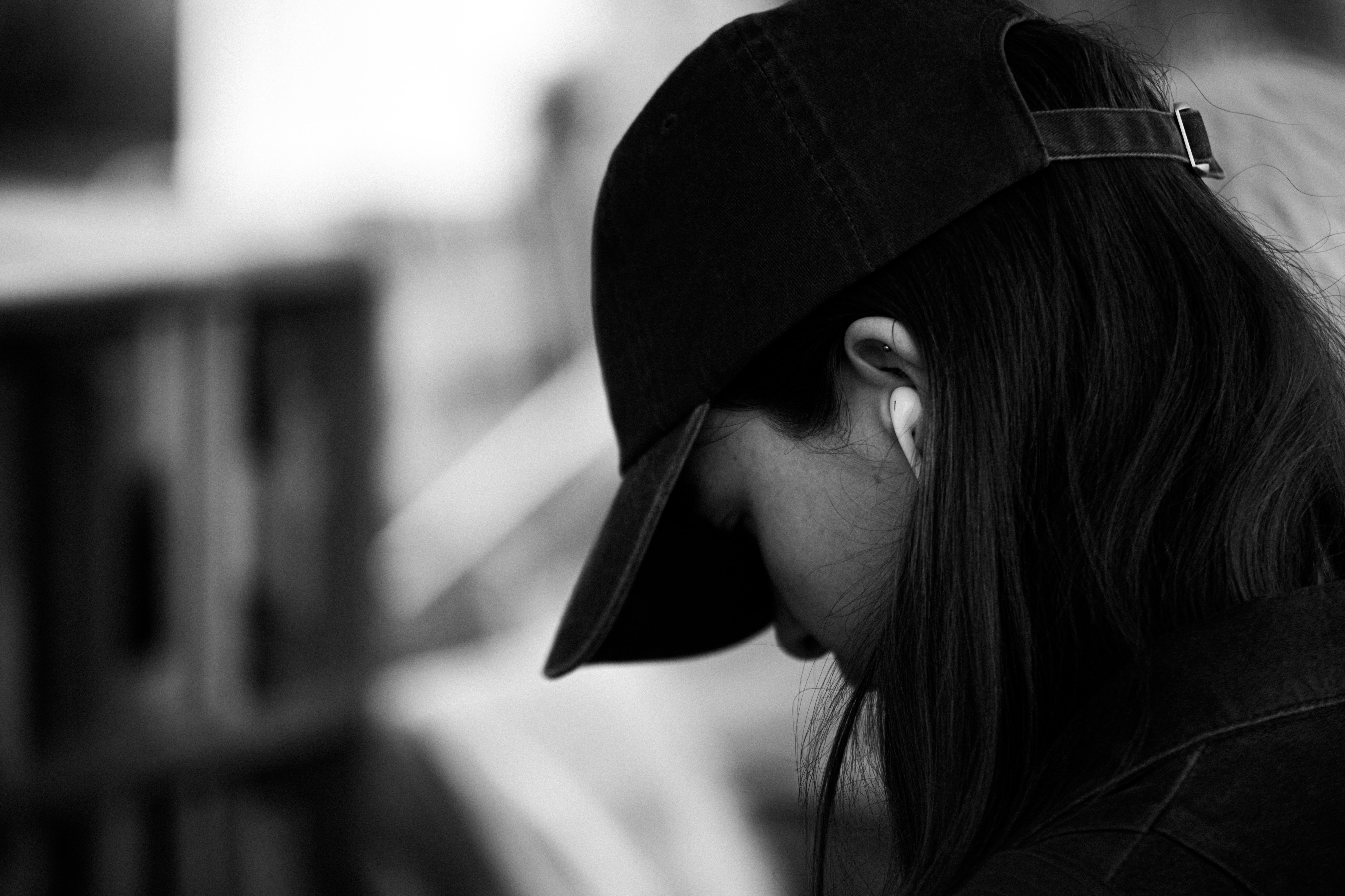 Artistic black-and-white portrait of a young woman wearing a cap and earbuds, exuding an urban lifestyle mood.
