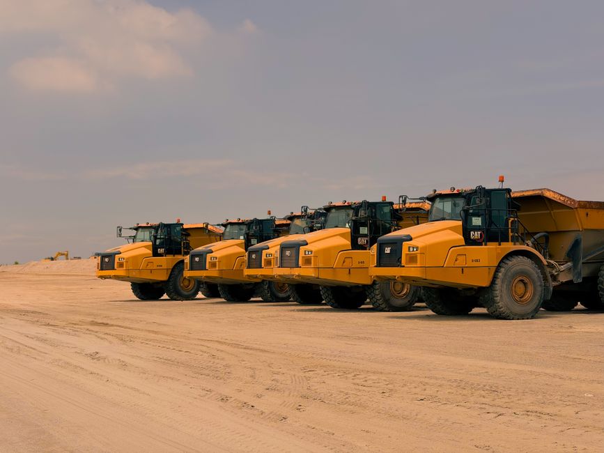 Caterpillar Inc. (CAT): The 100-Year-Old Industrial Giant Quietly Becoming an AI-Infrastructure Power Play 3 Row of heavy-duty dump trucks parked on a sandy construction site under a clear sky.