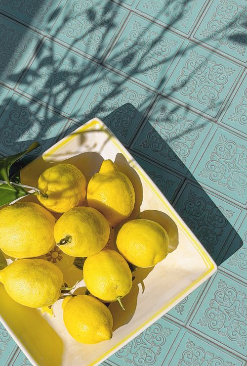 Free Vibrant yellow lemons in a ceramic bowl casting shadows on teal tile, under bright sunlight. Stock Photo