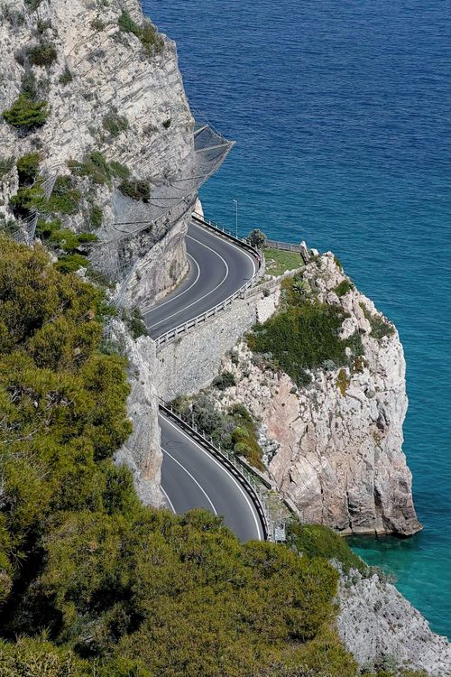 Free Winding coastal road carved into cliffs with azure sea, ideal for travel and adventure imagery. Stock Photo