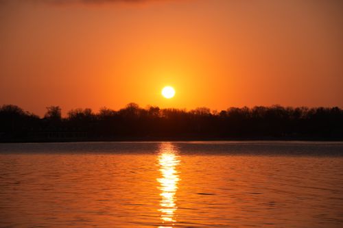 Free Beautiful sunset reflecting over a peaceful lake with silhouetted trees. Stock Photo
