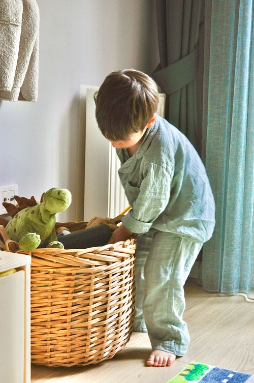 Free Young boy organizing toys in a wicker basket in a sunlit bedroom setting. Stock Photo