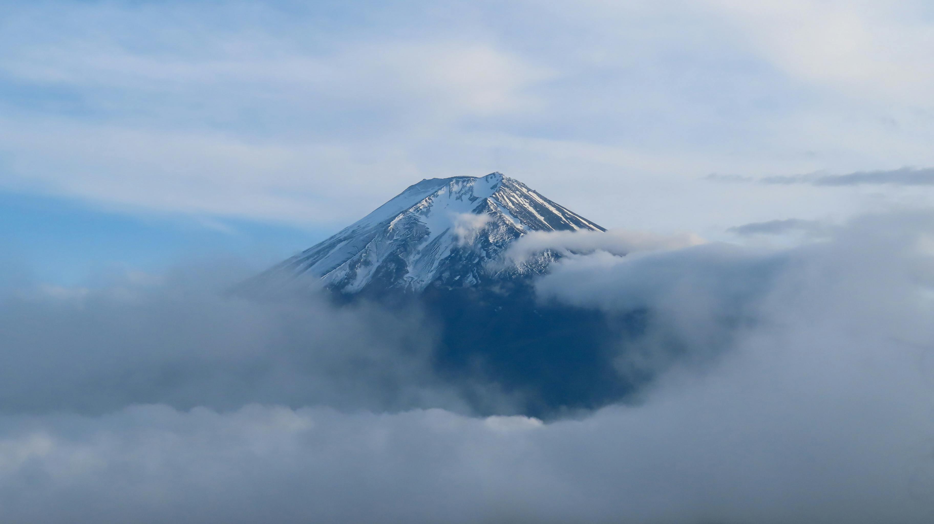 Majestic view of Mount Fuji with its snow-capped peak surrounded by clouds under a clear blue sky.