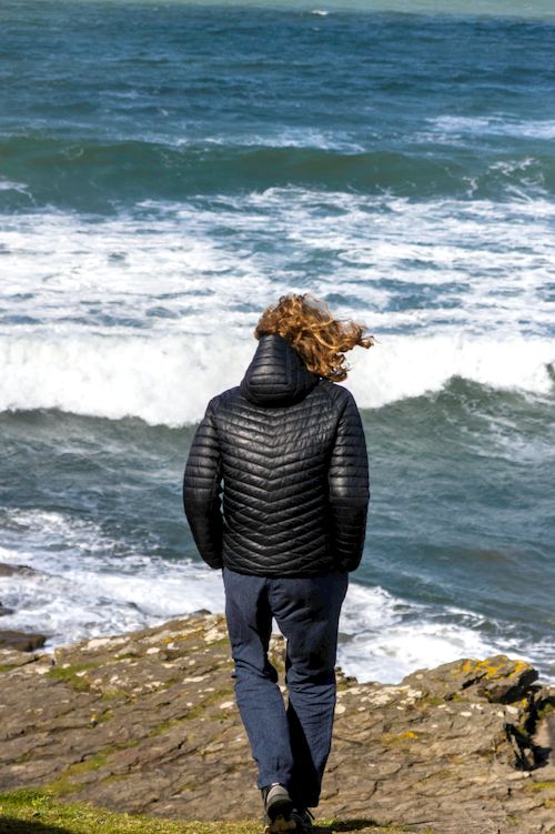 Free A person walks along the rocky coast of Little Haven, Wales, with waves crashing against the shore. Stock Photo