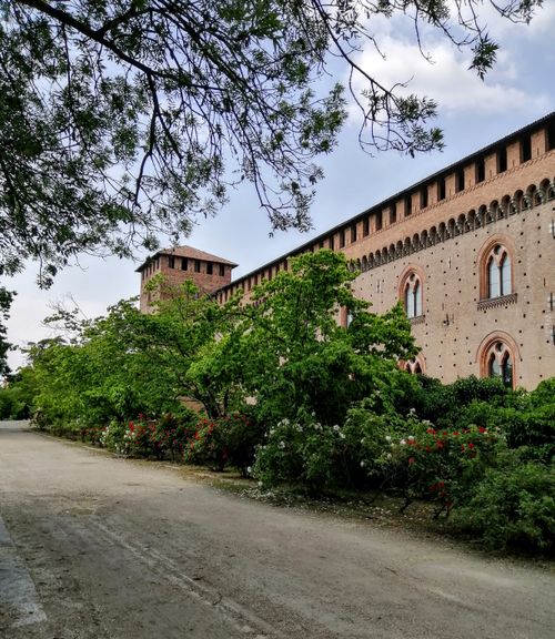 Free Charming view of a medieval castle in Pavia, Italy with lush greenery and a serene pathway. Stock Photo