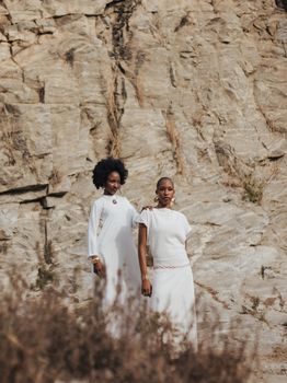 Two women in white attire posing against a rocky backdrop in nature, exuding elegance and strength.