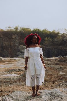 A woman in a white dress stands confidently in a natural, open setting.