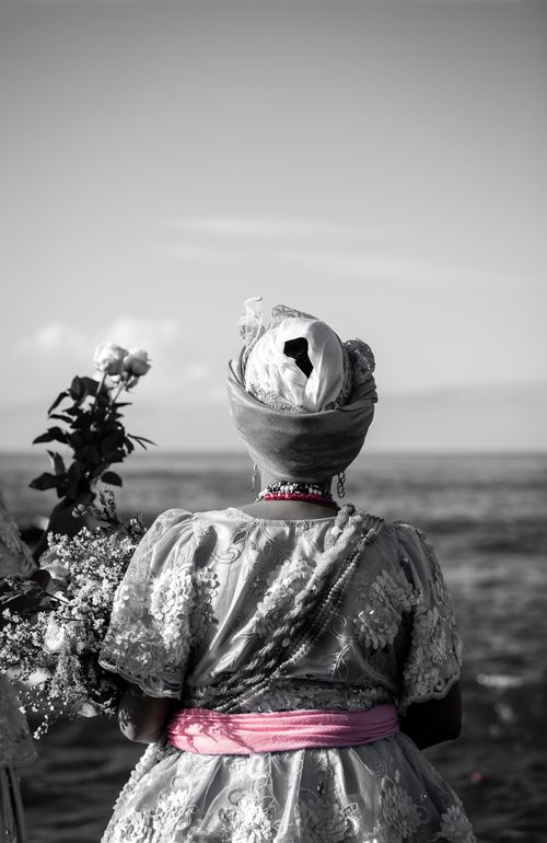 Free A Baiana woman in traditional attire stands by the ocean in Salvador, Brazil. Grayscale with pink details. Stock Photo