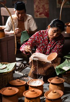 Indonesian woman and man preparing traditional meal with clay pots, showcasing cultural heritage.