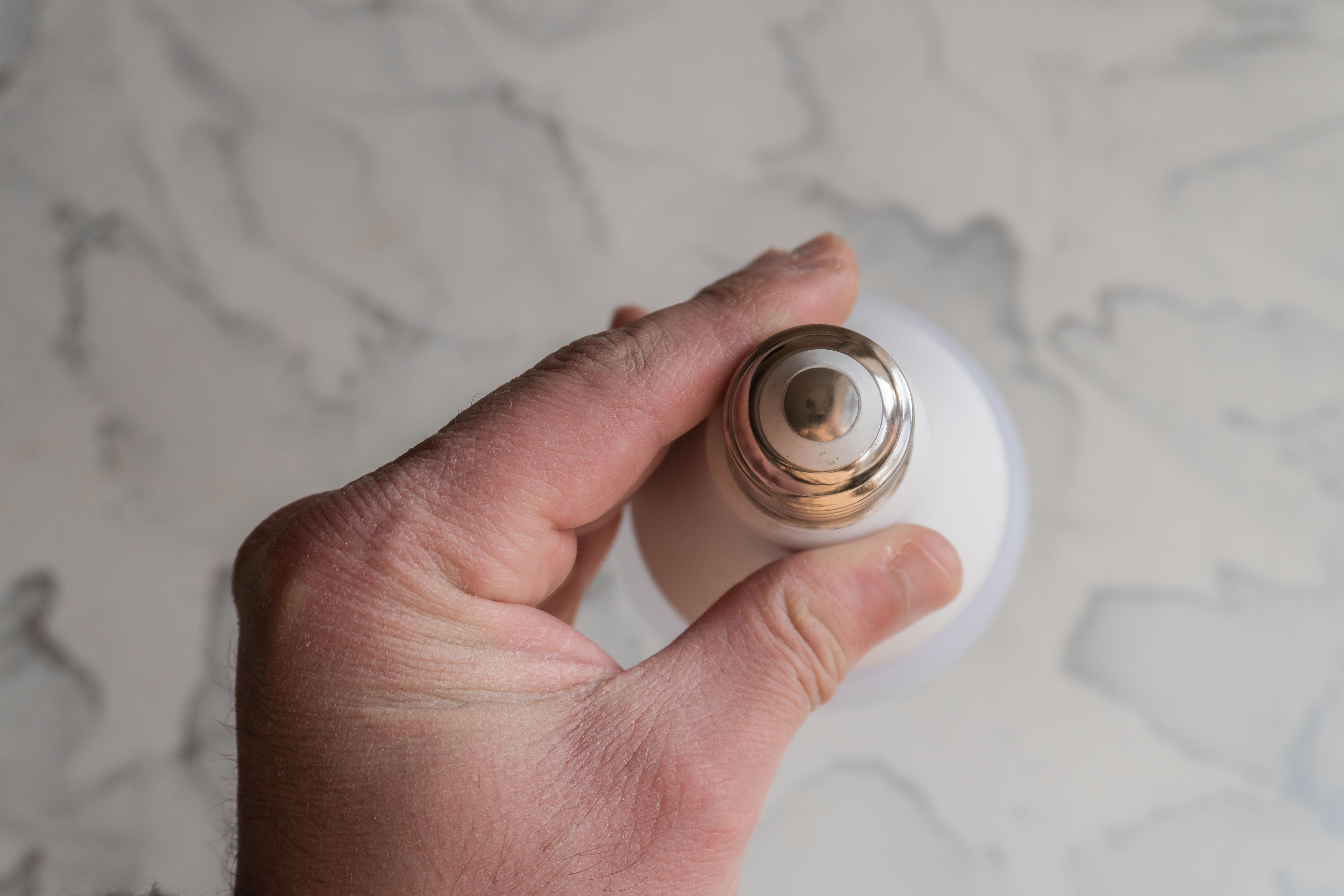 A close-up of a hand holding a light bulb against a marble surface, showing an abstract style.