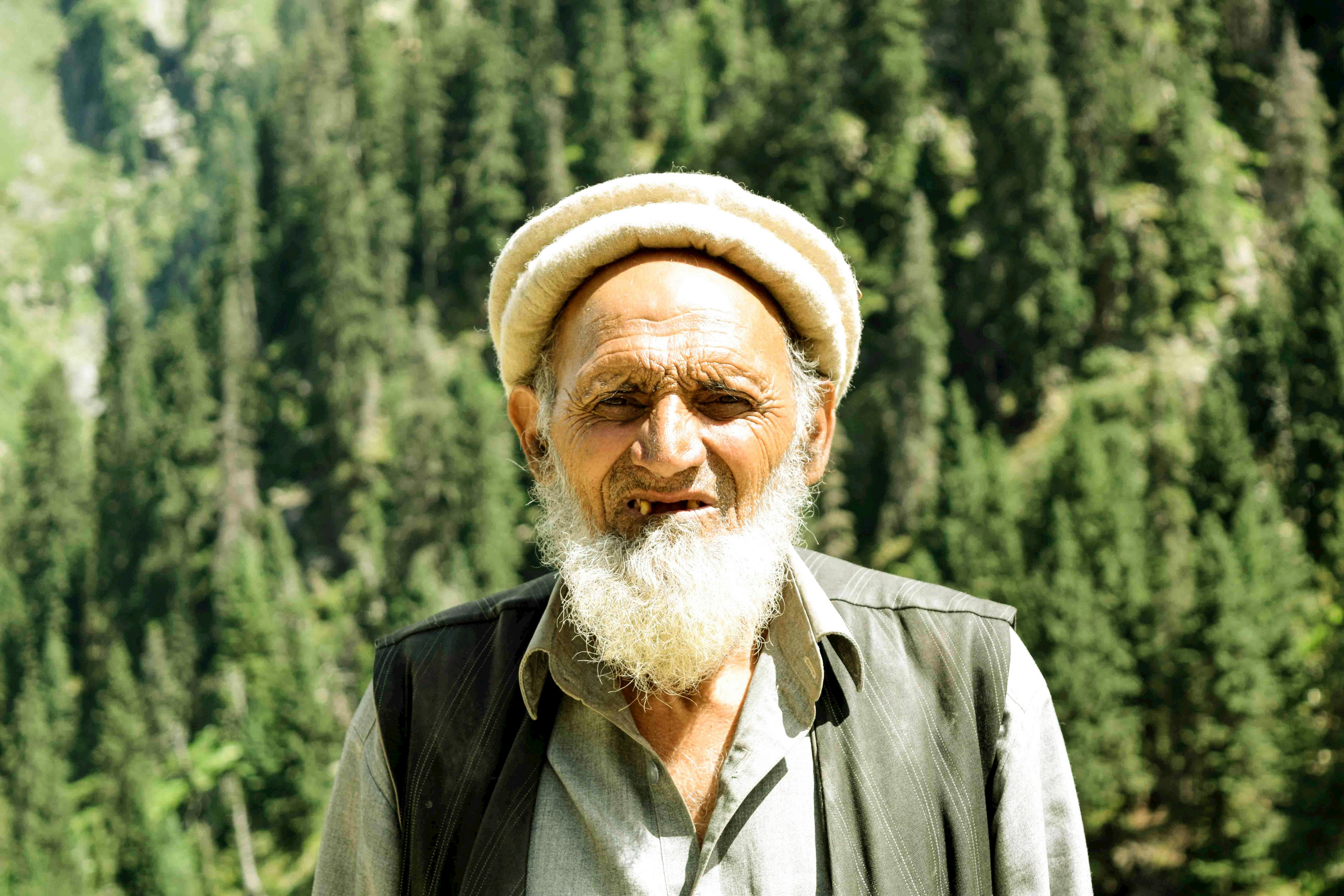 Portrait of an elderly man with a white beard and traditional pakol hat in Chail, Pakistan.