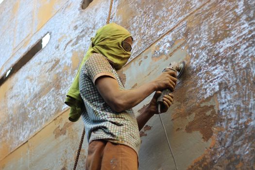 A worker using a grinder to polish rusted metal, wearing protective clothing outdoors.