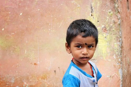 Free A thoughtful young child standing against a weathered wall, gazing with curiosity. Stock Photo