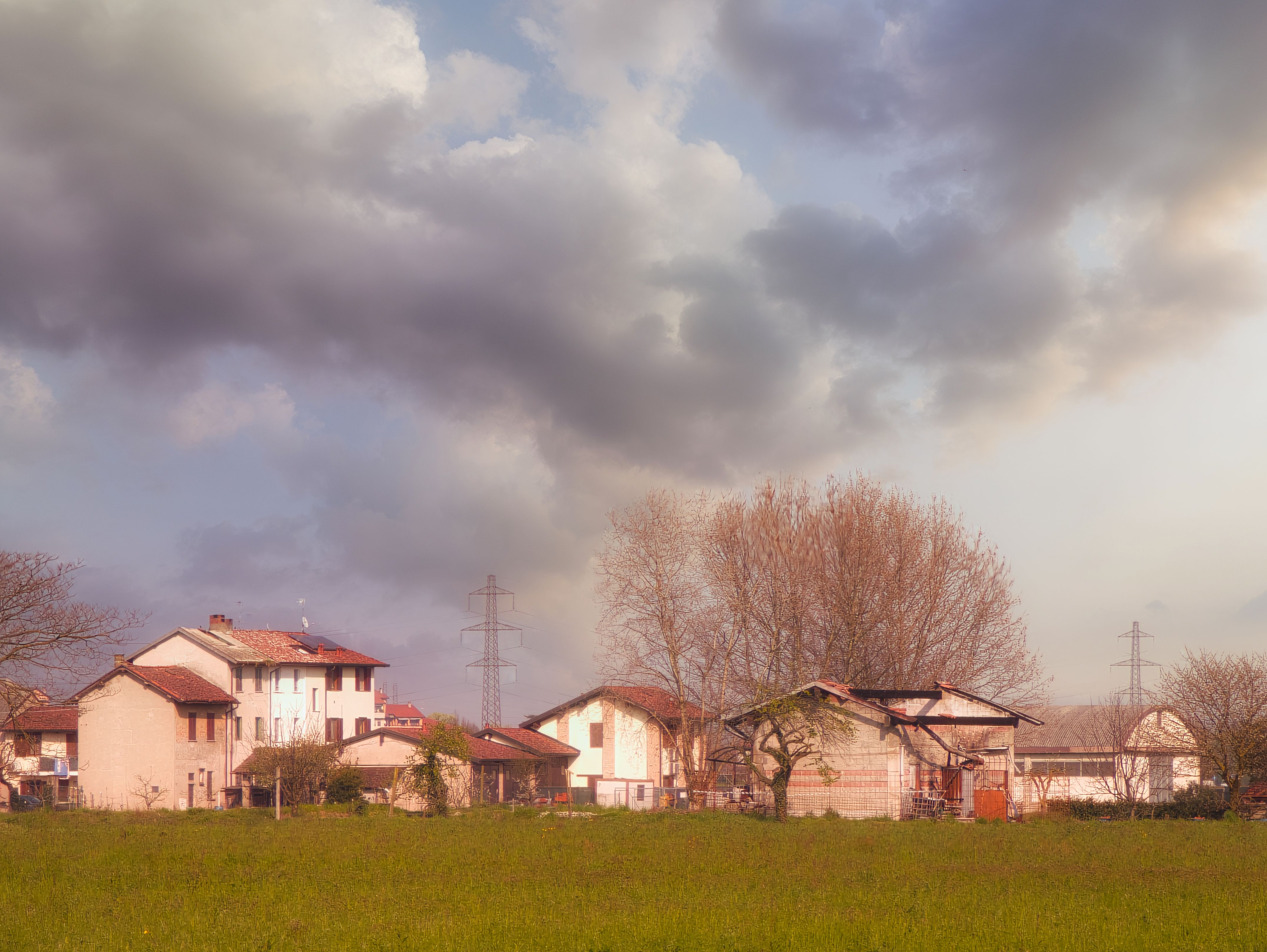 A tranquil Italian rural landscape in Caponago with houses under a dramatic cloudy sky.