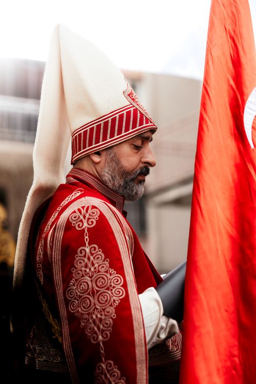 Free Man in traditional Turkish outfit holding a flag during a cultural parade outdoors. Stock Photo