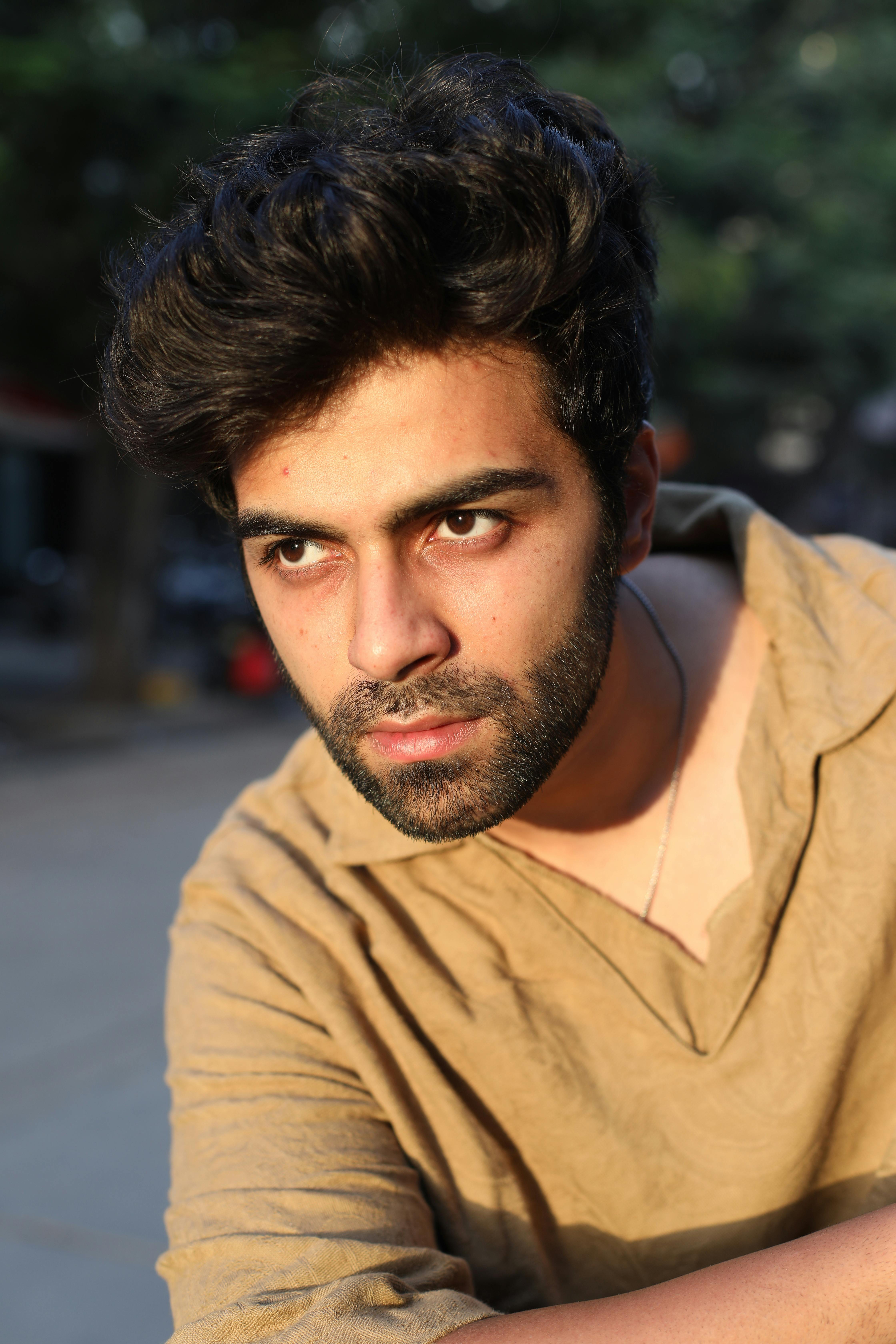 Close-up outdoor portrait of a pensive young adult man in warm sunlight.