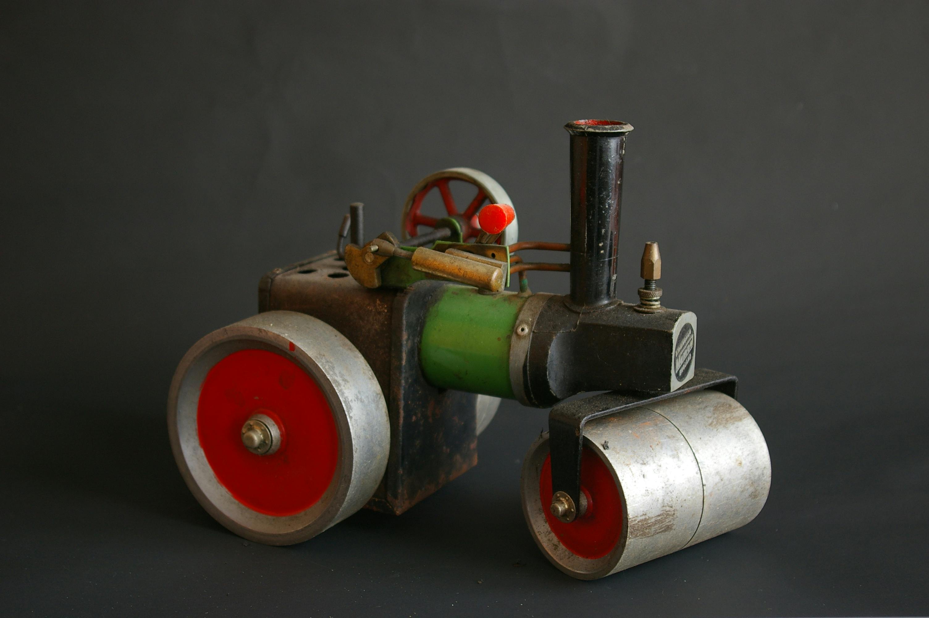 Close-up of a vintage toy steam roller with red wheels and detailed components against a dark backdrop.