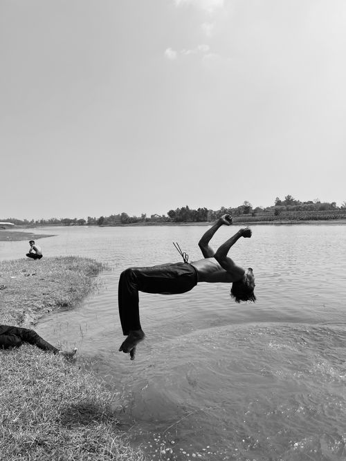 Free A young man performs a flip by a riverside, capturing a moment of joy and freedom. Stock Photo