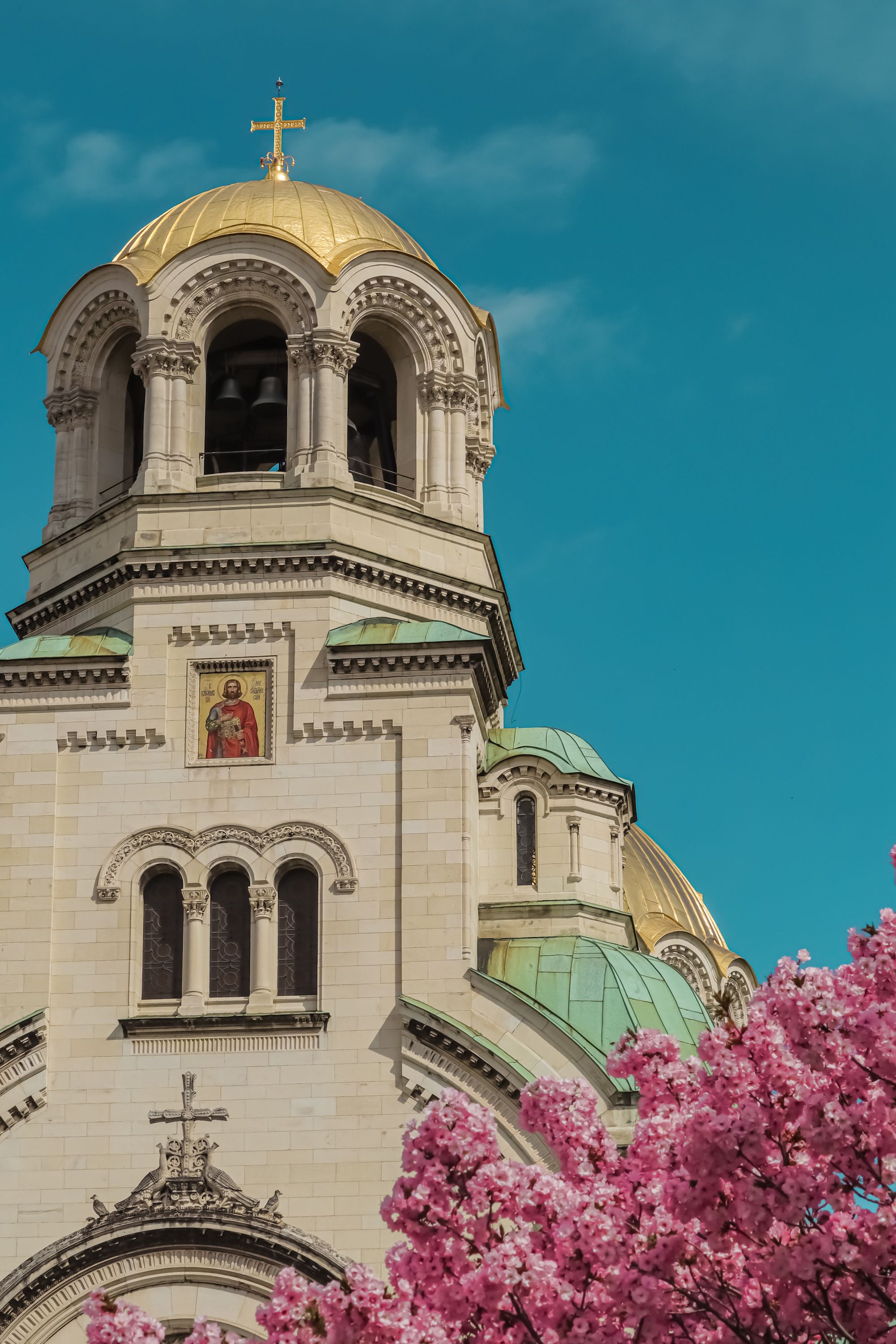 A cathedral with golden domes and spring blossoms under a clear blue sky.