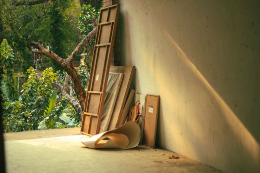 An art studio corner with wooden frames and paper, illuminated by afternoon sunlight, conveying creativity.