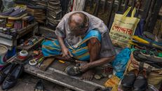 An elderly cobbler mending shoes in a vibrant Dhaka street market, Bangladesh.