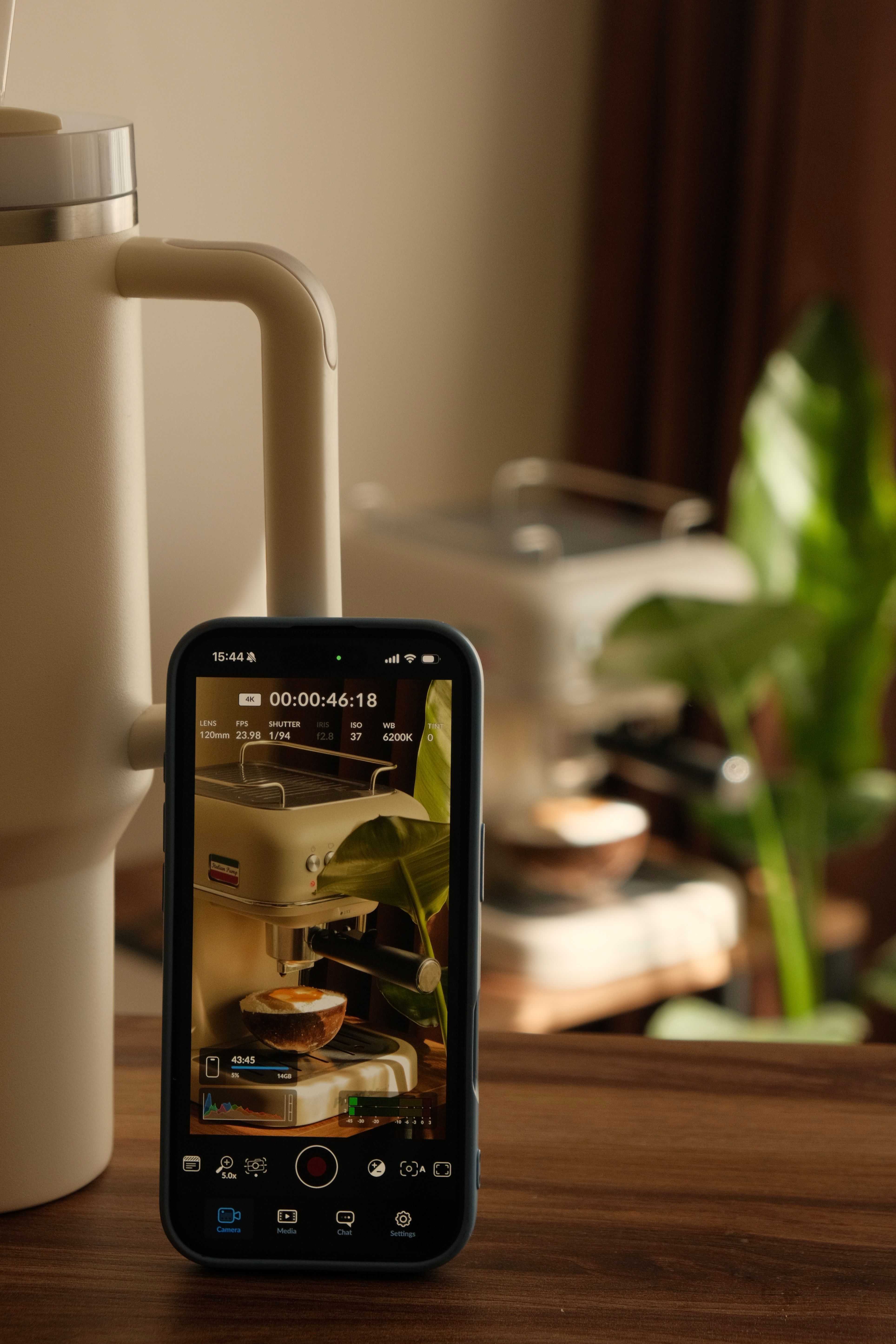Smartphone recording a coffee machine in a cozy kitchen setting with plants.
