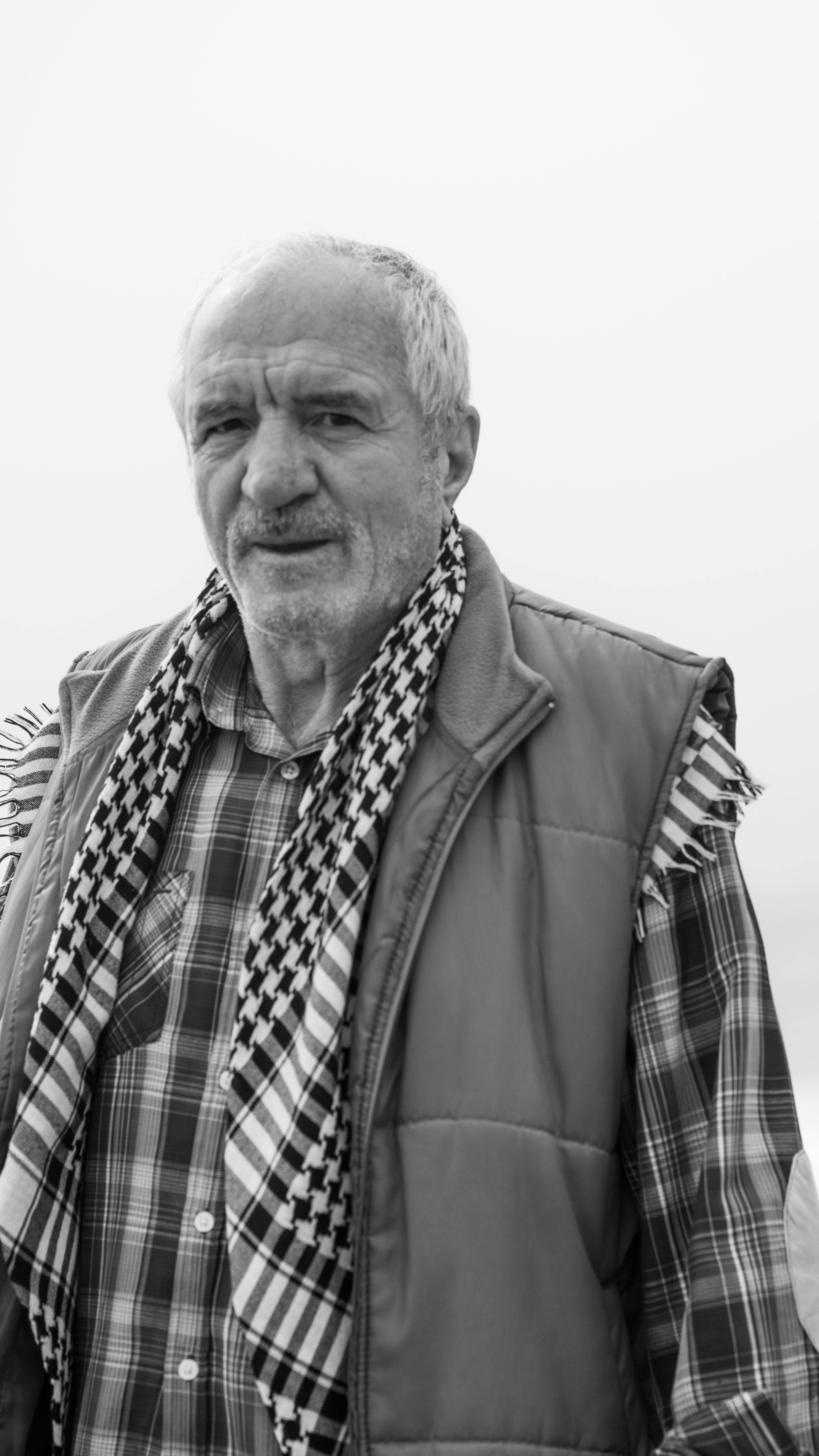 Black and white portrait of a senior man wearing a plaid shirt and vest, looking thoughtful.