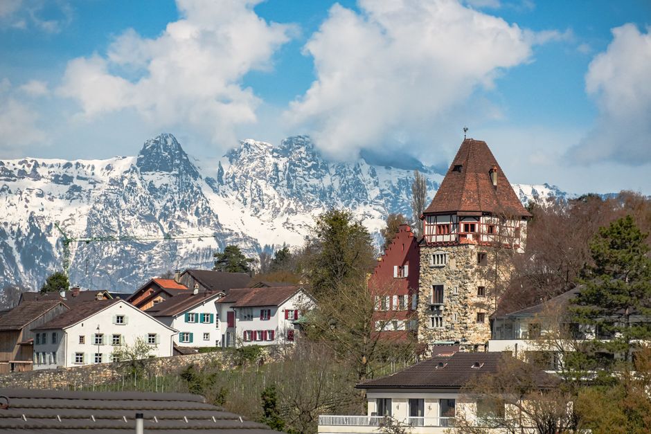 Charming village scene in Balzers, Liechtenstein, featuring traditional houses and stunning snow-capped Alps.