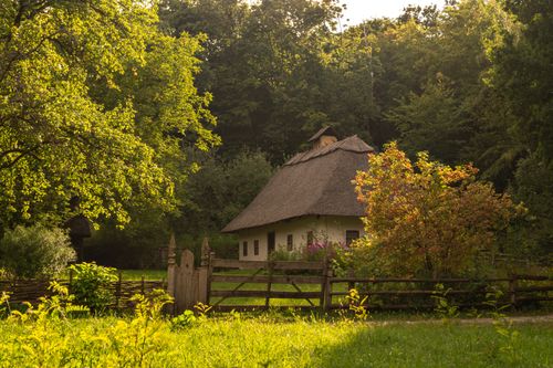Free Picturesque view of a traditional thatched-roof house surrounded by lush greenery and wooden fence in Kyiv, Ukraine. Stock Photo