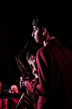 Side view of young musicians playing saxophones on stage in low light setting.