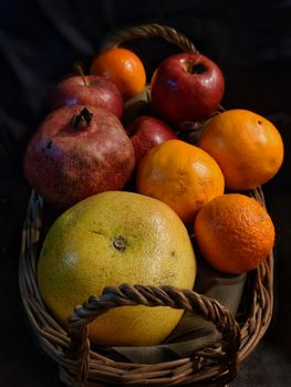 A wicker basket filled with fresh pomegranates, apples, oranges, and grapefruit.