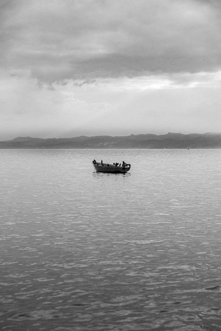 Fotomural Una fotografía serena en blanco y negro de un barco en aguas calmadas con montañas al fondo, Berat, Albania.