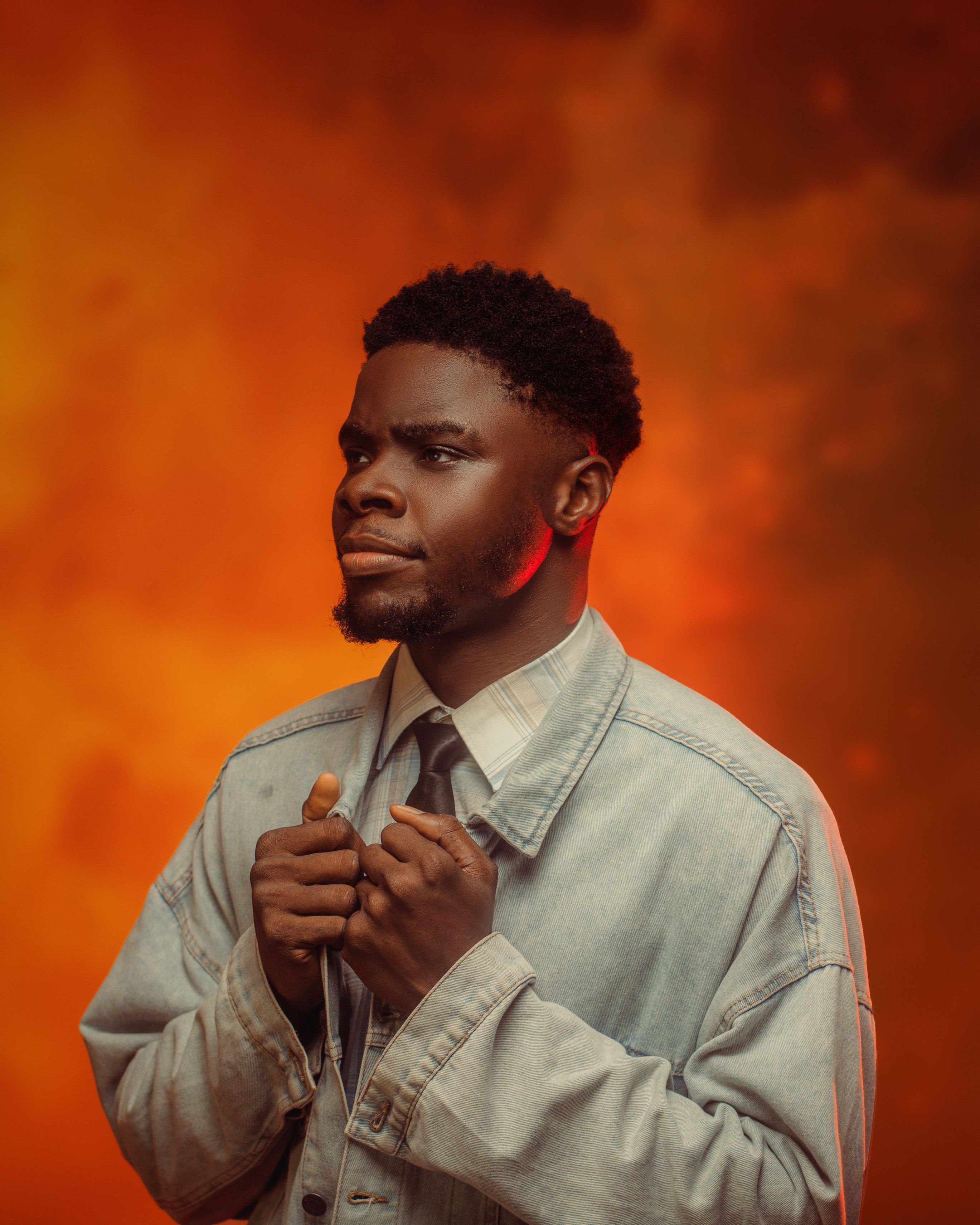 A contemplative man in a denim jacket with an orange sky background.