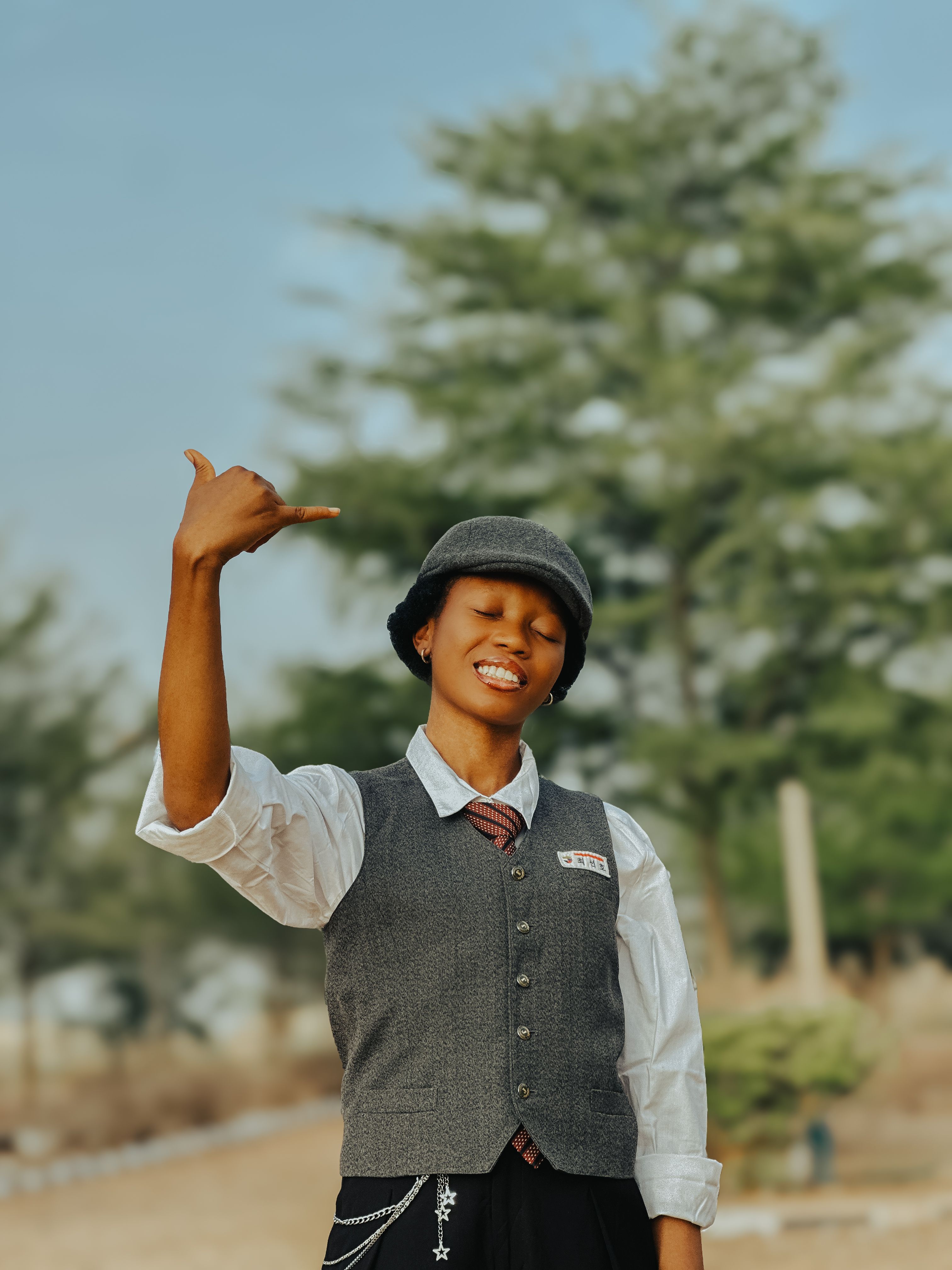 Young woman in vest and cap gesturing outdoors with a smile on a sunny day.