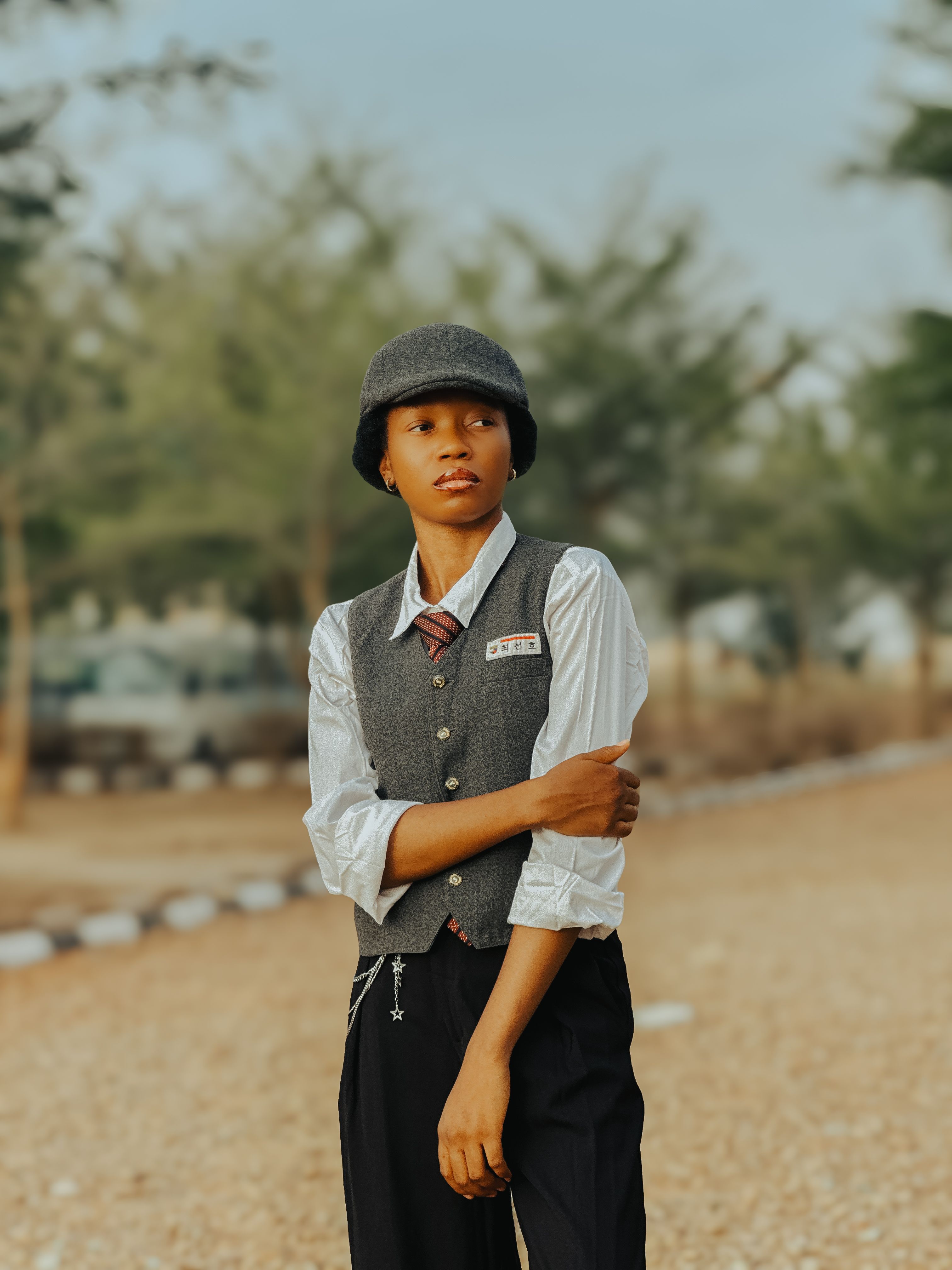 A stylish young adult in casual attire poses outdoors on a sunny day.