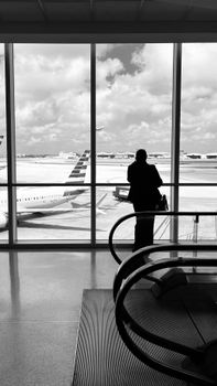 Silhouette of a traveler at an airport window overlooking planes on the tarmac.