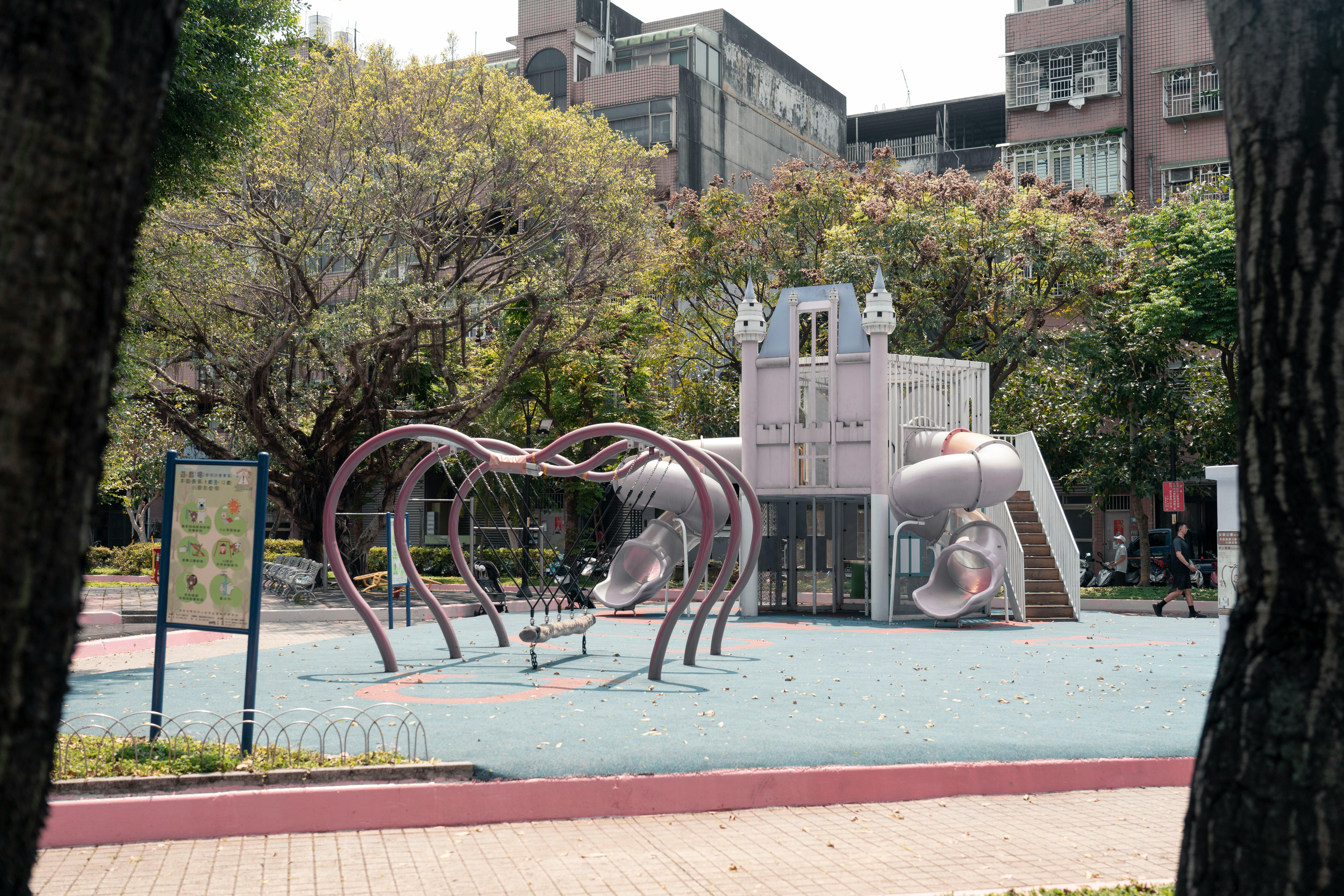 A modern playground in a Taipei park with slides and climbing structures, surrounded by trees.