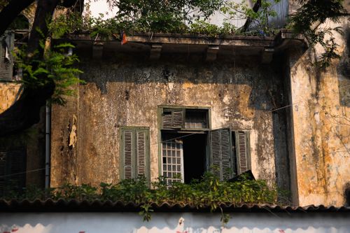 Free Vintage building facade with open wooden shutters, textured walls, and greenery in warm daylight. Stock Photo