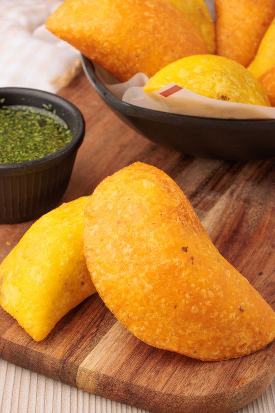 Crisp orange-yellow fried corn empanadas on a wooden board with herb aji sauce