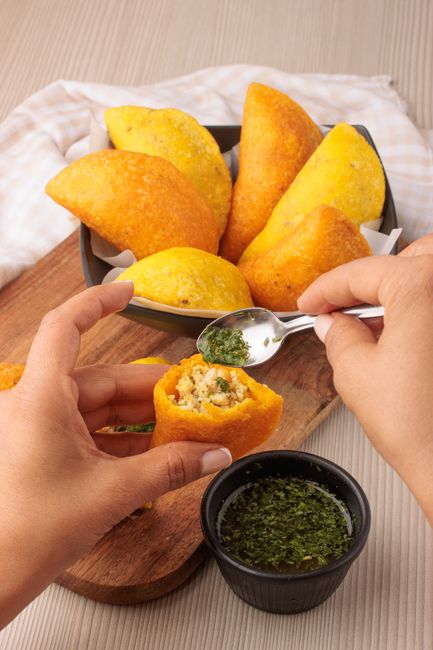 Close-up of Colombian empanadas being garnished with fresh herb sauce, highlighting traditional flavors.