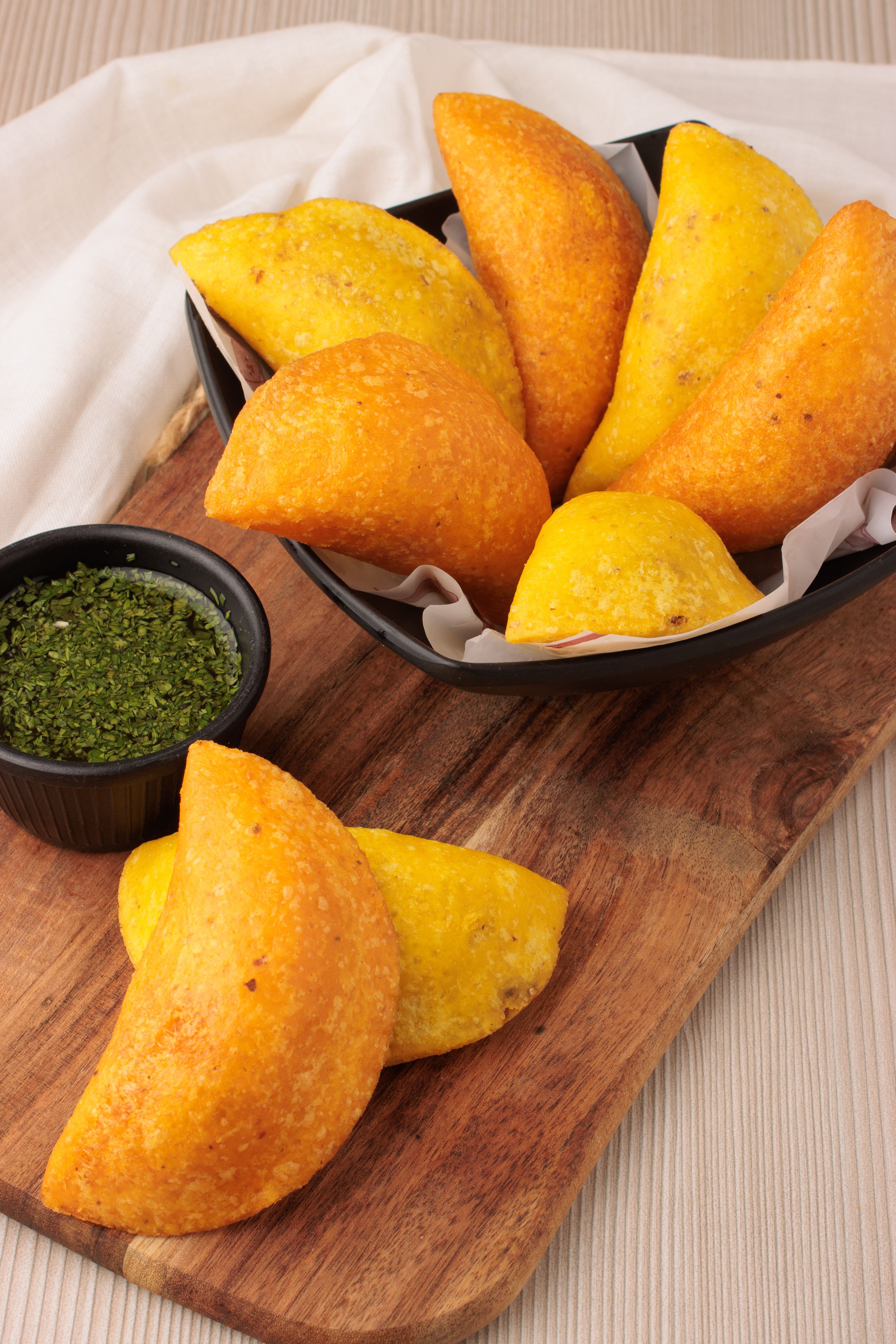 Gratuit Empanadas colombiennes servies sur une planche en bois avec une sauce verte en accompagnement, représentant la cuisine traditionnelle latino-américaine. Photos