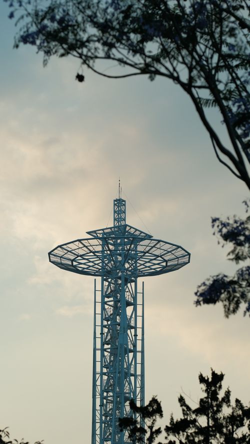 Free A modern communication tower set against a twilight sky with silhouettes of trees and clouds. Stock Photo