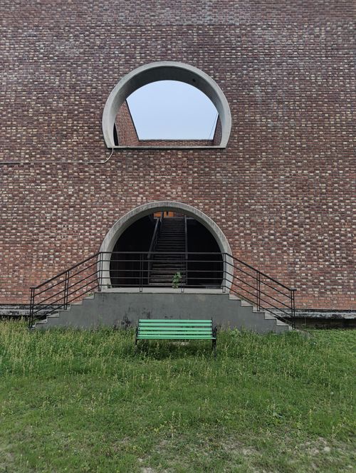 Free A striking brick building features two circular openings with a staircase and a green bench outside. Stock Photo