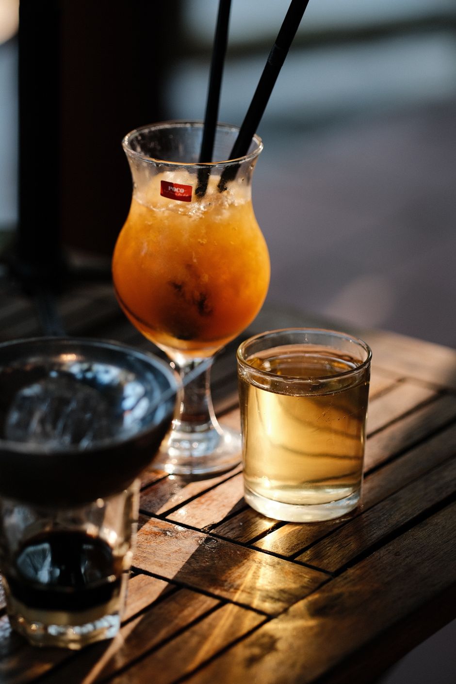 Three refreshing cocktails in various glasses on a wooden table in natural light.