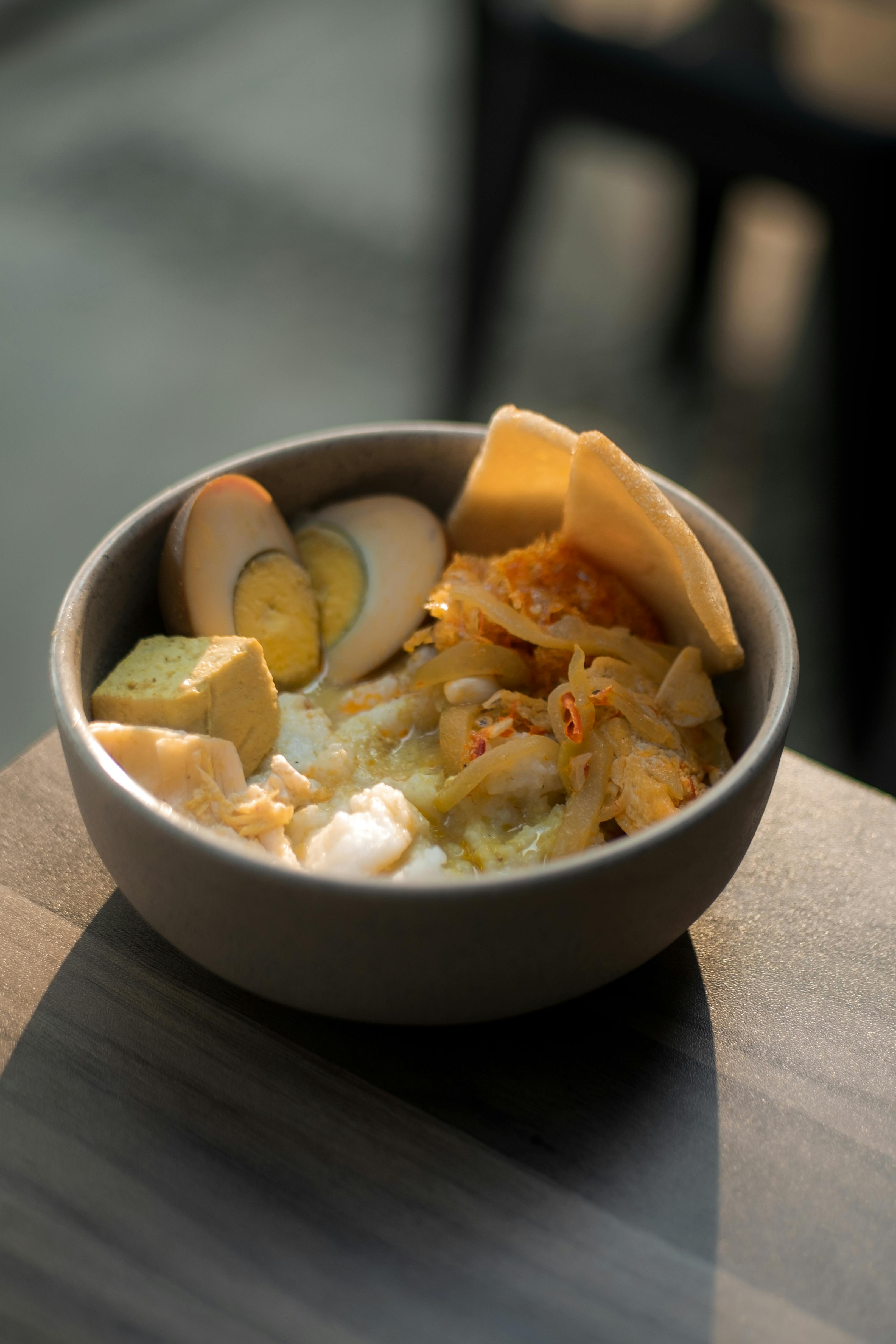 Savor a traditional bowl of Indonesian lontong with egg, tofu, and crackers under warm morning light.